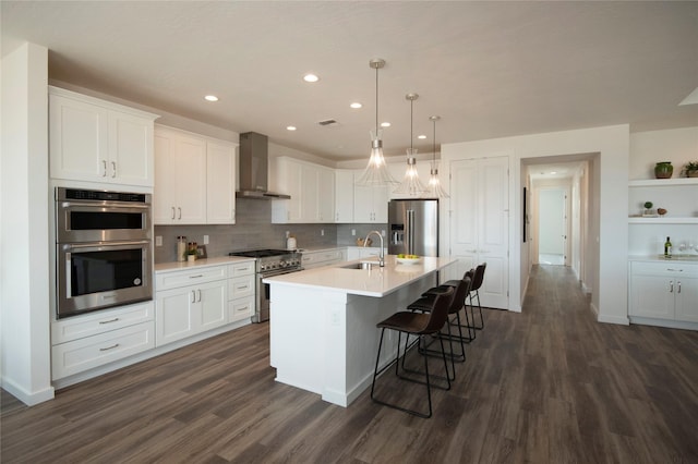 kitchen featuring sink, high end appliances, an island with sink, white cabinets, and wall chimney exhaust hood