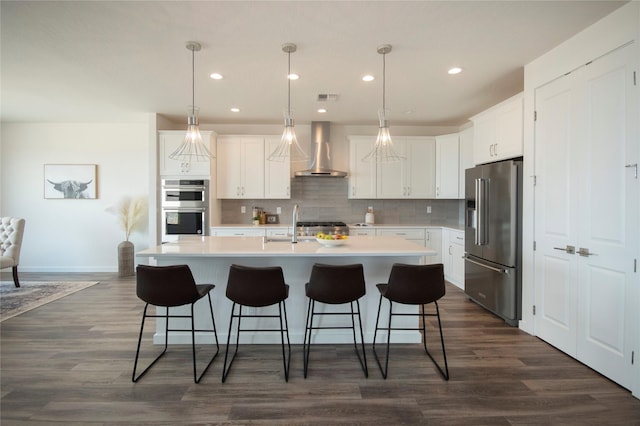 kitchen with white cabinets, stainless steel appliances, an island with sink, and wall chimney exhaust hood