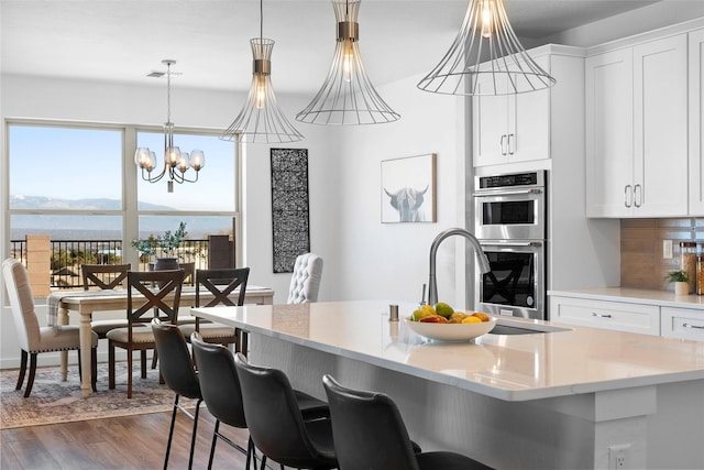 kitchen featuring double oven, white cabinetry, hanging light fixtures, a water view, and dark wood-type flooring