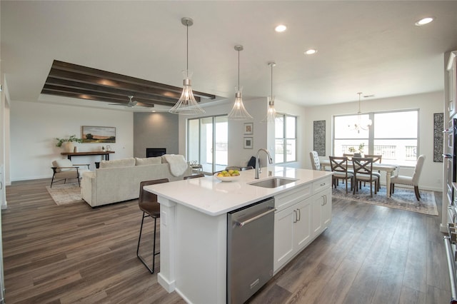 kitchen featuring decorative light fixtures, dishwasher, an island with sink, sink, and white cabinets