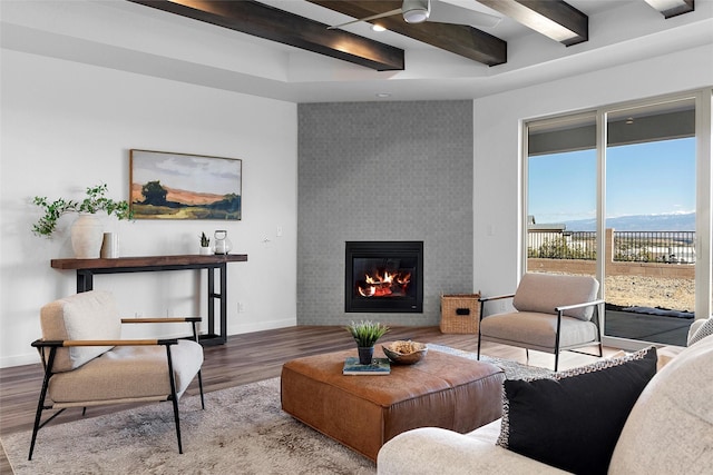 living room with wood-type flooring, a large fireplace, ceiling fan, a mountain view, and beam ceiling