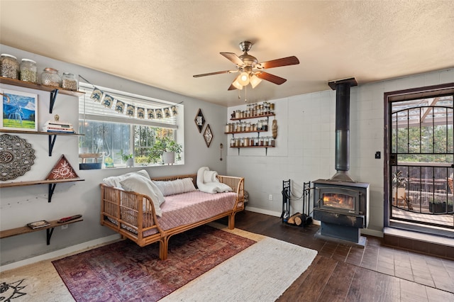 bedroom featuring a wood stove, ceiling fan, dark hardwood / wood-style flooring, and a textured ceiling