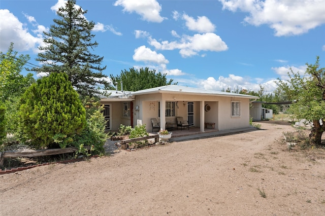 rear view of property featuring dirt driveway and stucco siding