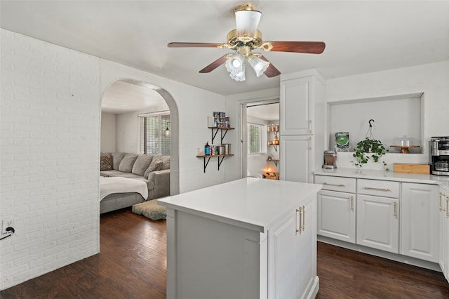 kitchen featuring brick wall, ceiling fan, dark wood-type flooring, white cabinets, and a kitchen island