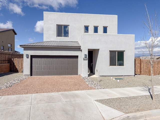 view of front facade featuring an attached garage, fence, stucco siding, metal roof, and driveway