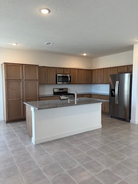 kitchen featuring appliances with stainless steel finishes, a textured ceiling, sink, a center island with sink, and dark stone countertops