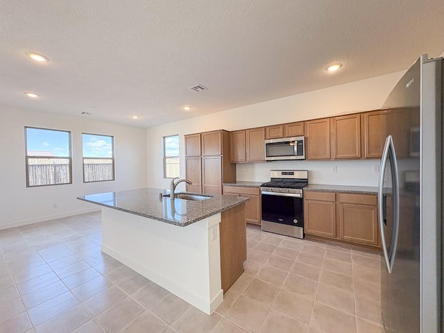 kitchen featuring dark stone countertops, light tile patterned floors, a sink, appliances with stainless steel finishes, and brown cabinets