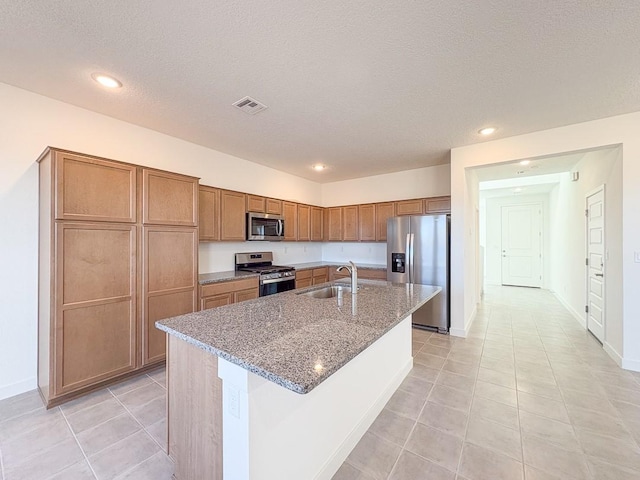 kitchen with visible vents, a center island with sink, a sink, light stone counters, and appliances with stainless steel finishes