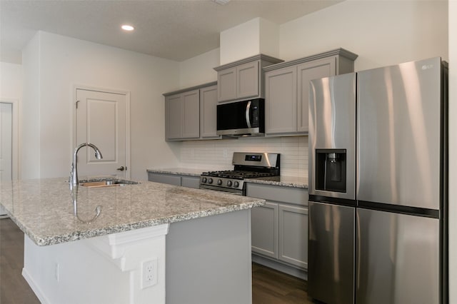 kitchen featuring light stone countertops, appliances with stainless steel finishes, an island with sink, and sink