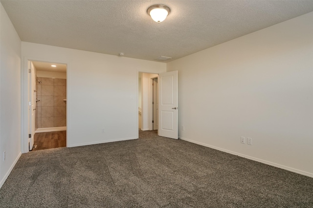 unfurnished bedroom with a textured ceiling, dark colored carpet, and connected bathroom