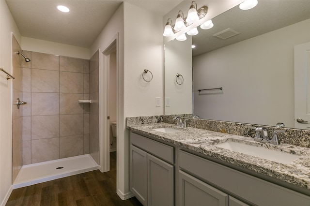 bathroom featuring toilet, vanity, a tile shower, and hardwood / wood-style floors