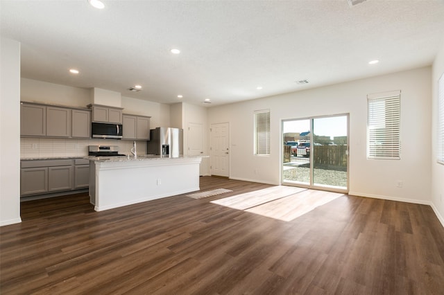 kitchen with appliances with stainless steel finishes, dark wood-type flooring, an island with sink, gray cabinets, and light stone counters