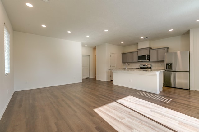 kitchen featuring a center island with sink, light stone countertops, gray cabinetry, stainless steel appliances, and dark hardwood / wood-style flooring