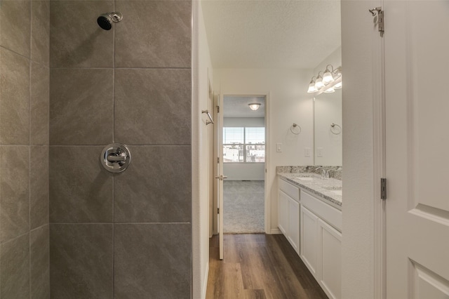 bathroom with hardwood / wood-style floors, vanity, and a tile shower