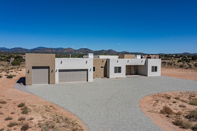 pueblo-style house with an attached garage, a mountain view, driveway, and stucco siding