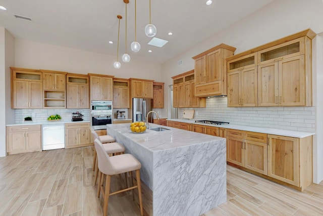 kitchen featuring decorative backsplash, a kitchen island with sink, sink, hanging light fixtures, and appliances with stainless steel finishes