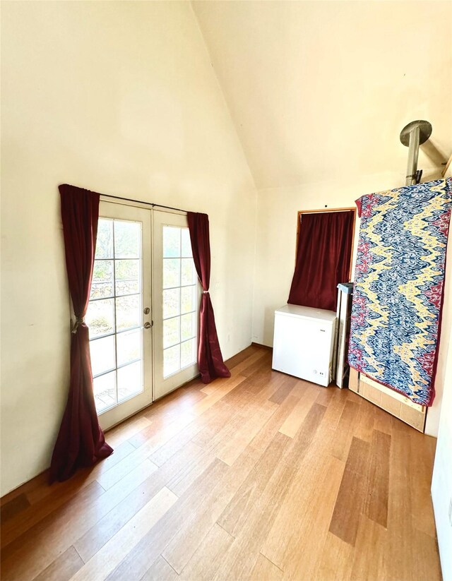 unfurnished bedroom with lofted ceiling, light hardwood / wood-style flooring, access to exterior, and french doors