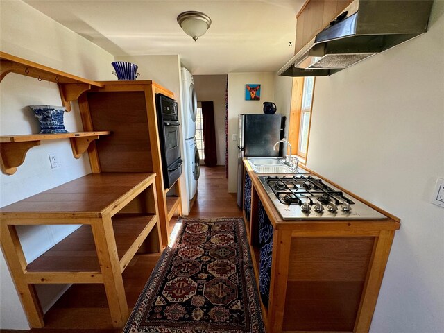 kitchen with stainless steel gas stovetop, wall chimney range hood, sink, washer / clothes dryer, and dark hardwood / wood-style flooring