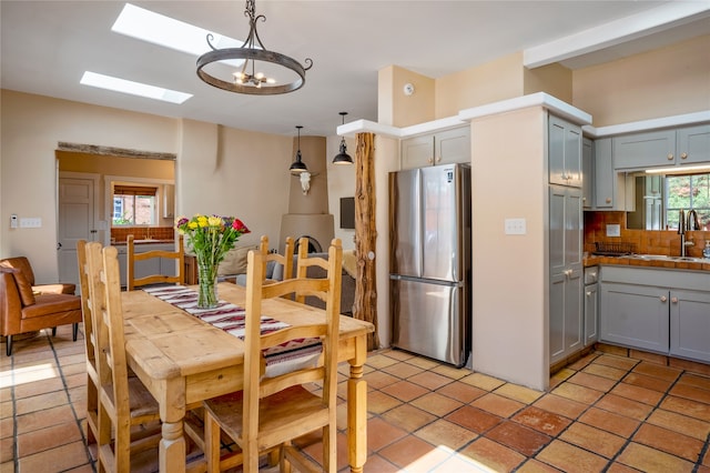 kitchen with stainless steel fridge, pendant lighting, backsplash, light tile patterned floors, and a skylight