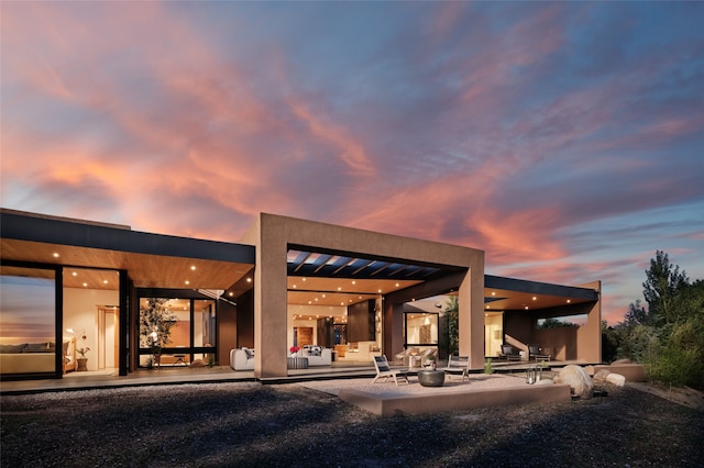 back house at dusk featuring a pergola and a patio area