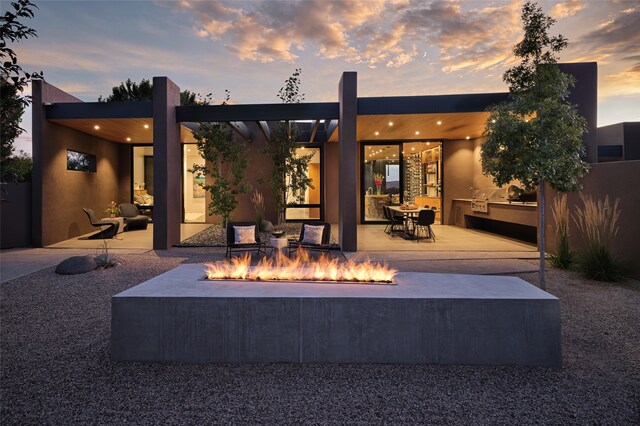 back house at dusk featuring a patio and a fire pit