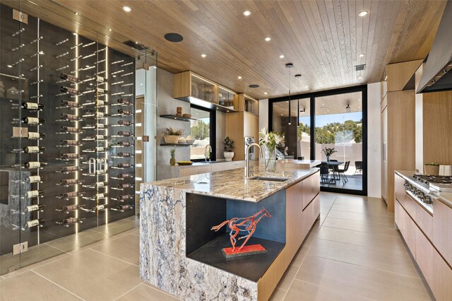 kitchen featuring sink, light stone counters, light tile patterned floors, wooden ceiling, and a large island with sink