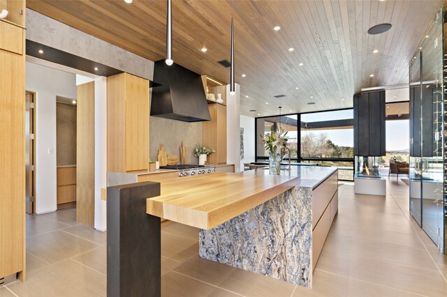 kitchen featuring expansive windows, wall chimney range hood, wooden ceiling, and a spacious island