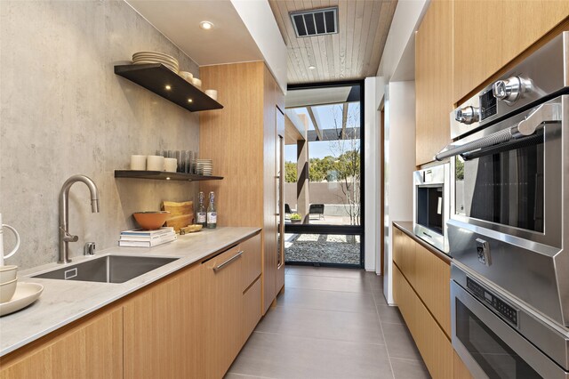 kitchen with light tile patterned flooring, sink, light stone counters, expansive windows, and stainless steel double oven