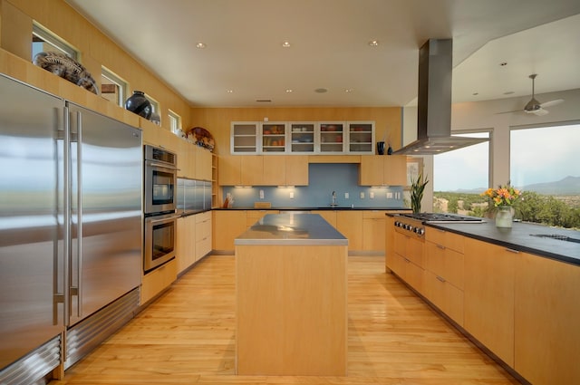 kitchen with light hardwood / wood-style flooring, appliances with stainless steel finishes, a center island, ceiling fan, and wall chimney exhaust hood