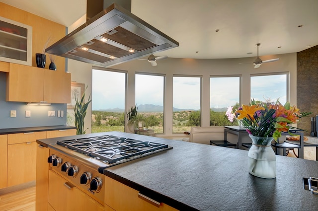 kitchen featuring light wood-type flooring, light brown cabinets, island range hood, ceiling fan, and stainless steel gas stovetop