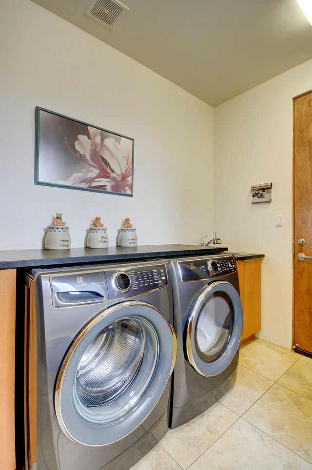 washroom with washing machine and dryer, light tile patterned flooring, and cabinets