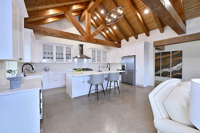 kitchen with wall chimney range hood, white cabinets, stainless steel appliances, and an island with sink