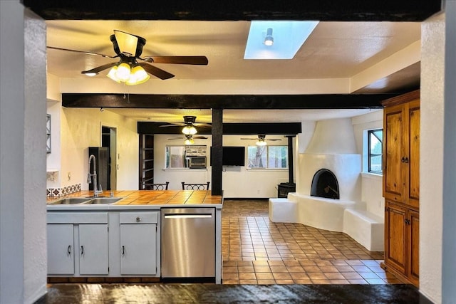 kitchen with tile counters, stainless steel dishwasher, a sink, and a healthy amount of sunlight