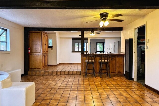 kitchen with a textured ceiling, a kitchen bar, kitchen peninsula, ceiling fan, and light tile patterned flooring