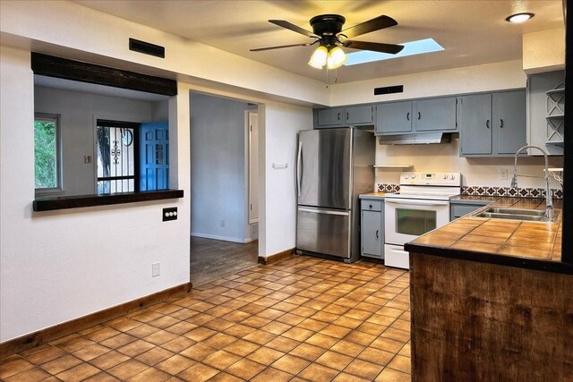 kitchen with stainless steel refrigerator, sink, a skylight, ceiling fan, and white range with electric cooktop