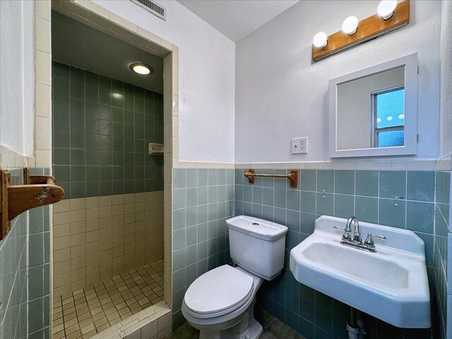 bathroom featuring tiled shower, tile walls, toilet, sink, and decorative backsplash