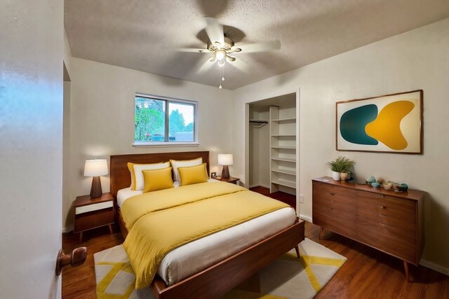 bedroom with a textured ceiling, dark hardwood / wood-style floors, a spacious closet, a closet, and ceiling fan