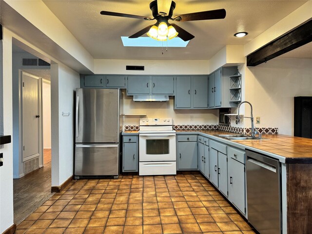 kitchen featuring appliances with stainless steel finishes, light hardwood / wood-style floors, sink, ceiling fan, and tile counters