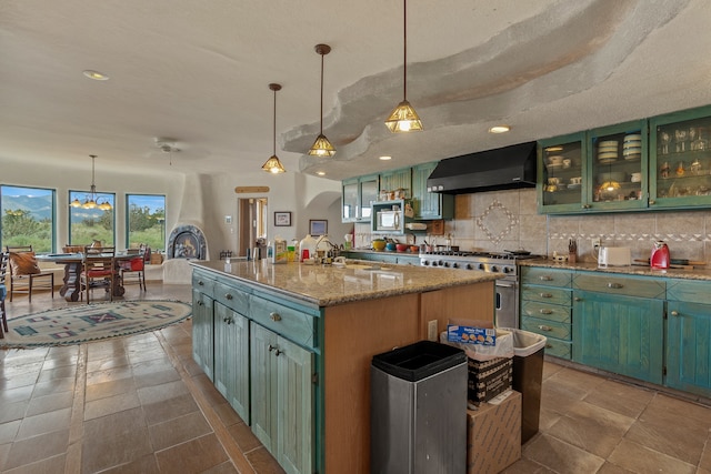 115 Waldo Mesa, Madrid, NM 87010 - kitchen featuring hanging light fixtures, a kitchen island with sink, high end range, light stone counters, and wall chimney range hood