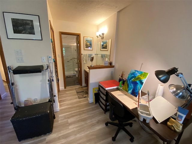 office with baseboards, light wood-type flooring, and a textured ceiling