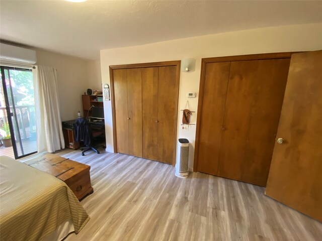 bedroom featuring multiple closets, a wall unit AC, access to outside, and light hardwood / wood-style floors