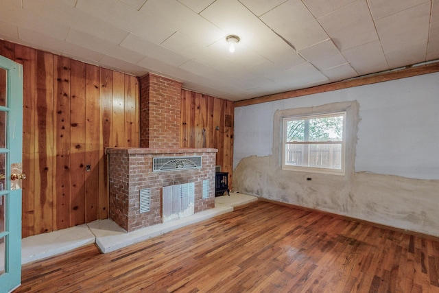 unfurnished living room with hardwood / wood-style flooring, a brick fireplace, and wood walls