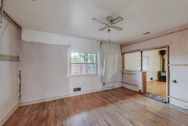 unfurnished room with a wood stove, light hardwood / wood-style flooring, and ceiling fan