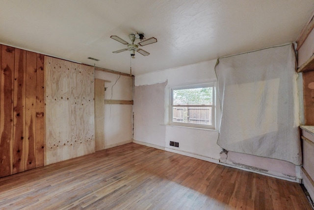 empty room featuring ceiling fan, wood walls, and light hardwood / wood-style floors