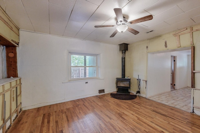 unfurnished living room with a wood stove, ceiling fan, and light hardwood / wood-style floors