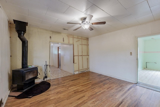 living room with ceiling fan, a wood stove, and light hardwood / wood-style floors