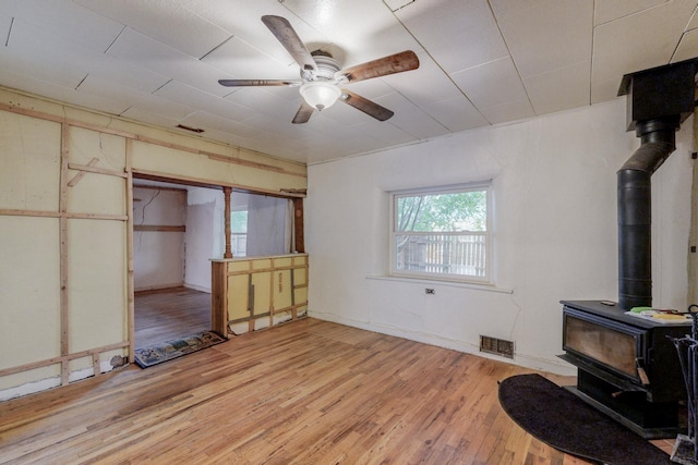 living room with ceiling fan, light wood-type flooring, and a wood stove