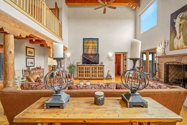 living room with beam ceiling, light wood-type flooring, ceiling fan, and a towering ceiling