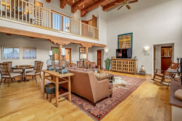 living room with wood ceiling, ceiling fan, beam ceiling, a towering ceiling, and light hardwood / wood-style flooring