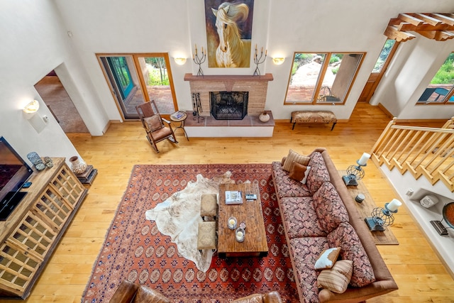 living room with a tiled fireplace, a towering ceiling, and light hardwood / wood-style flooring